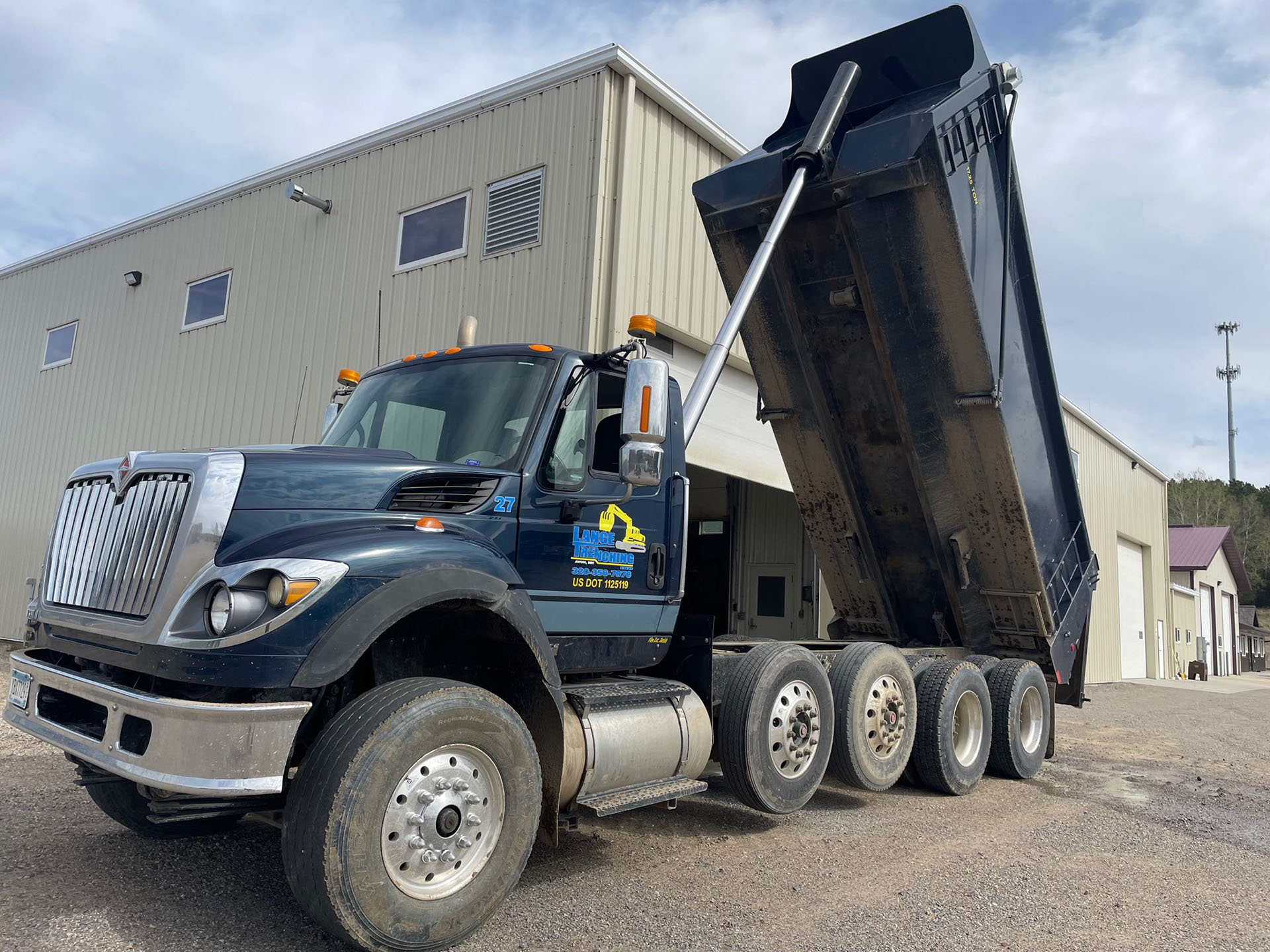 Road grader in the foreground smoothing a fresh layer of aggregate with an excavator in the background