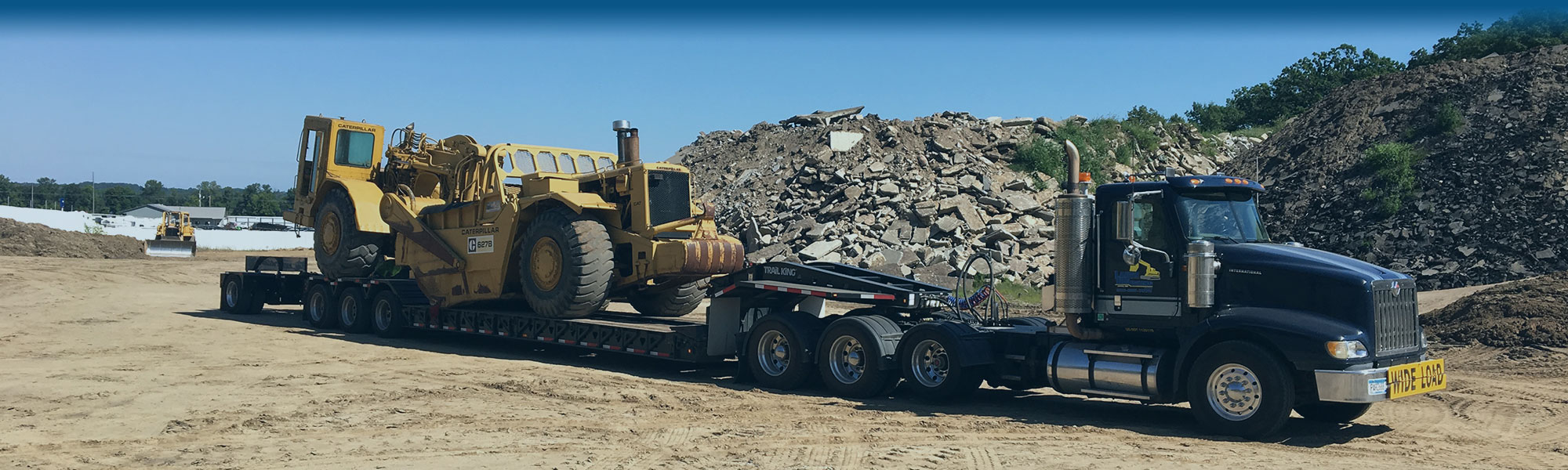 Lange Trenching semi tractor hauling a large peice of excavating equipment on a flatbed trailer